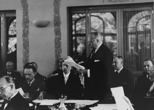 Myron Taylor addresses the International Conference on Refugees at Évian-les-Bains. James Grover McDonald is seated next to him. On the far right edge of the picture is Robert Thompson Pell, an assistant to Myron Taylor at State. The bloke looking down, twoth from left of Taylor, with a dark tie and moustache is Georges Coulon.
